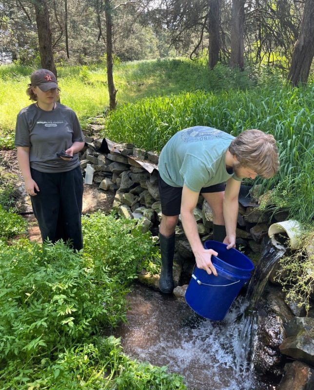 two students getting water samples from a creek