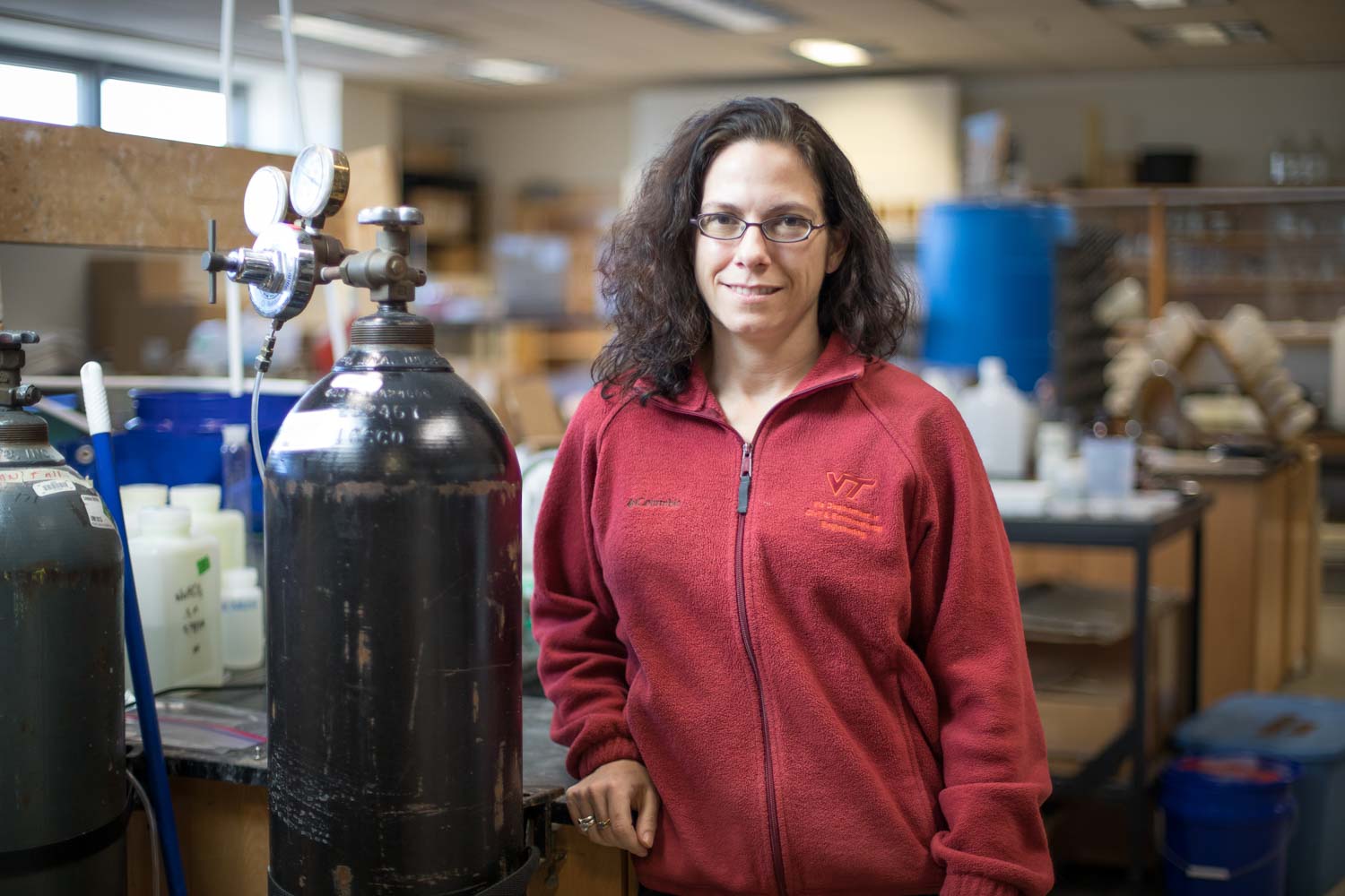 A woman leans on a lab table and smiles for a photo.